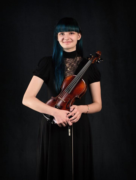 Madeline Pojar smiles as she holds her violin and bow. 