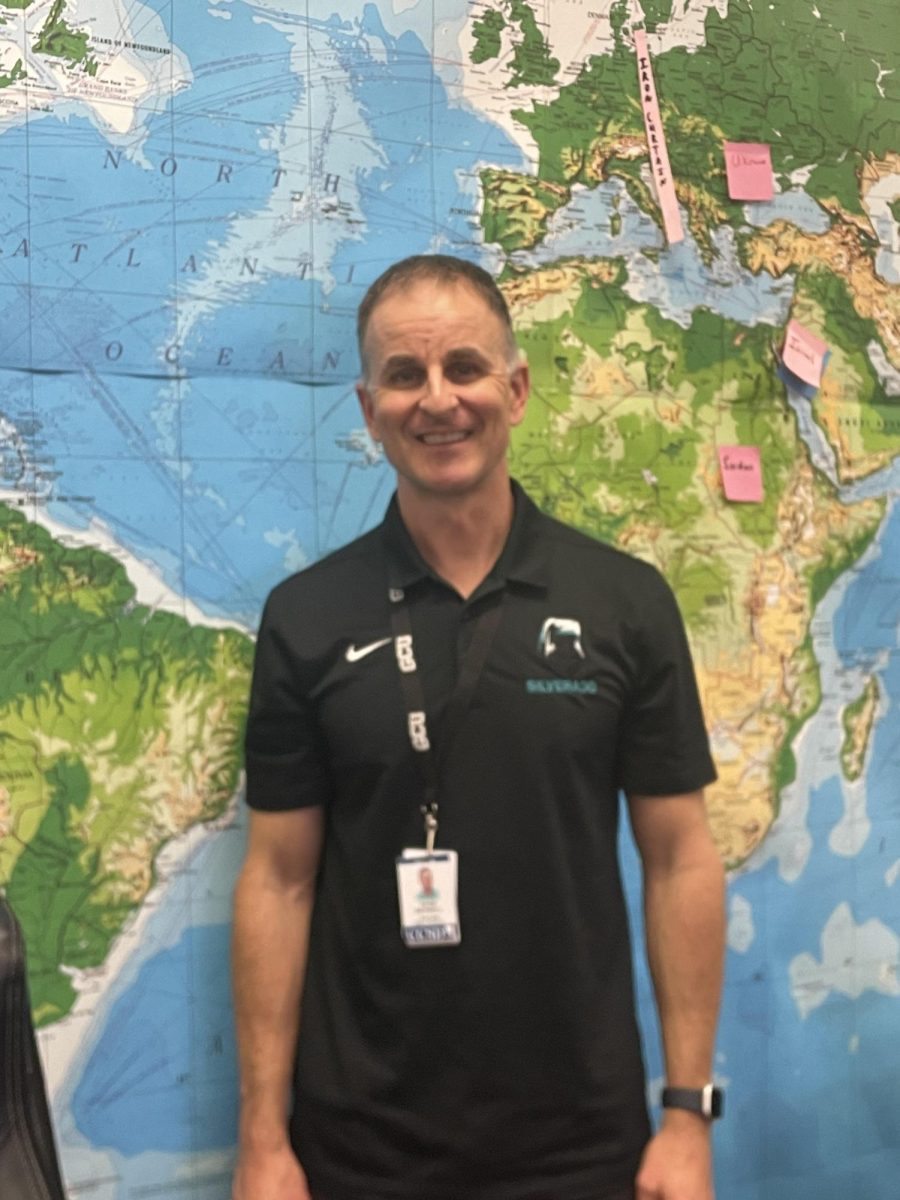 History teacher Adam Maxwell smiles in front of a world map. 